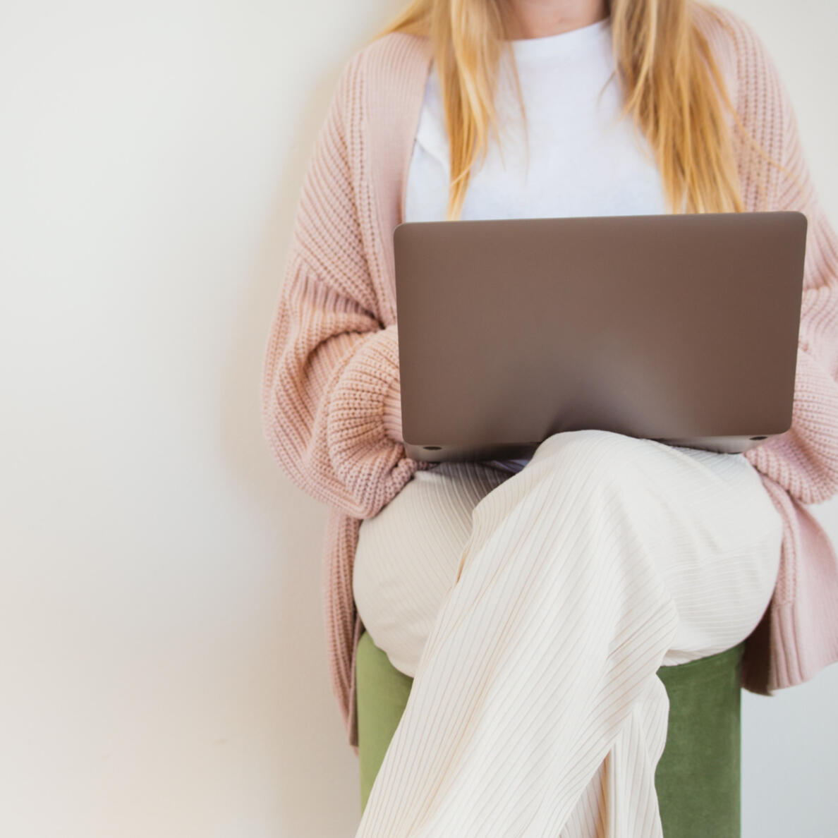 Career Support for Job Seekers - Woman sitting on a stool, legs crossed, with an open laptop on her lap.