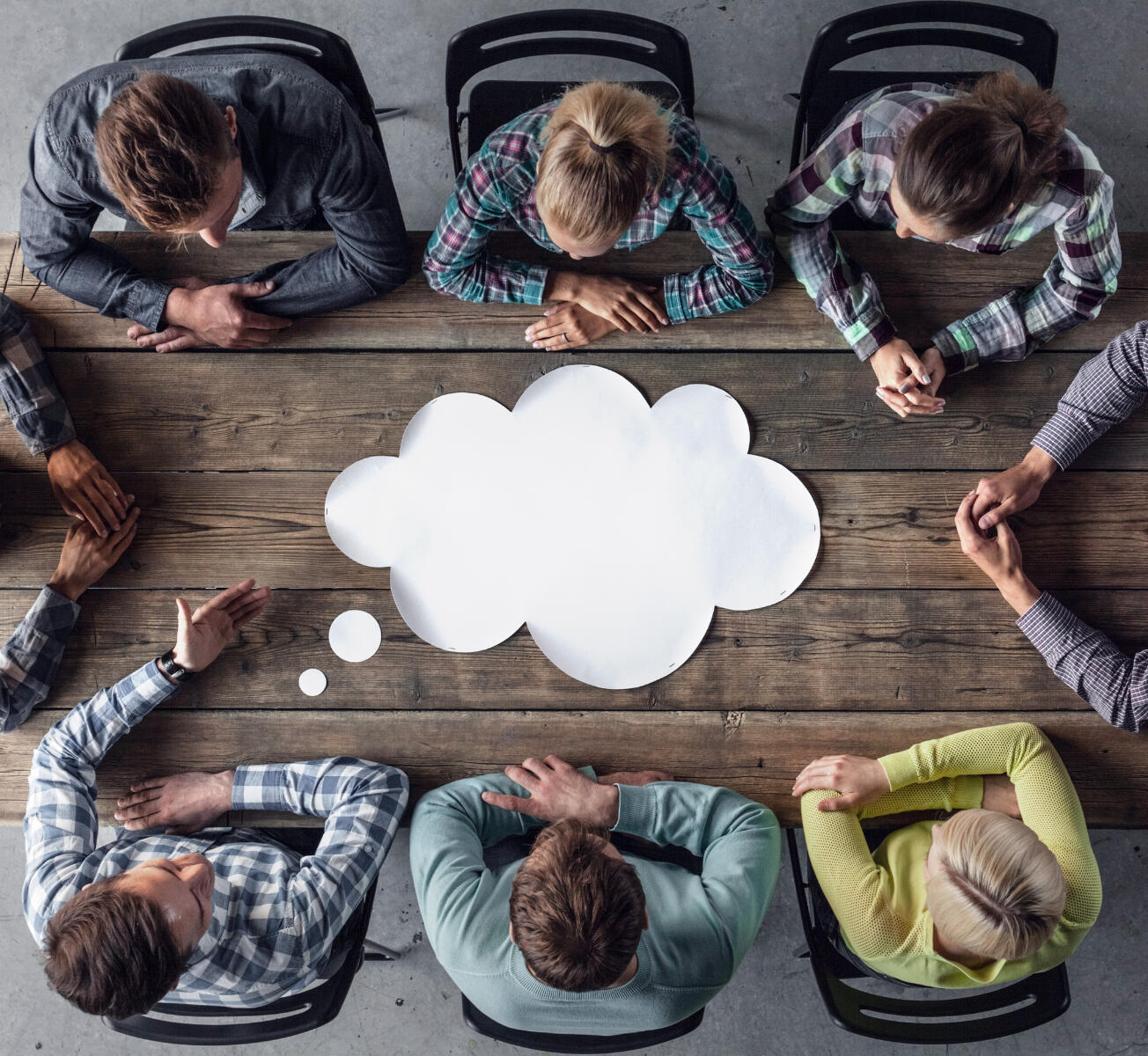 Career Support for Workplaces - Six individuals, with the hands of two more, sit at a wooden table with a gigantic thought cloud on it.